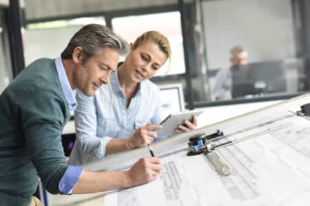A man and woman at a drafting table, creating blueprints for a property they co-own.