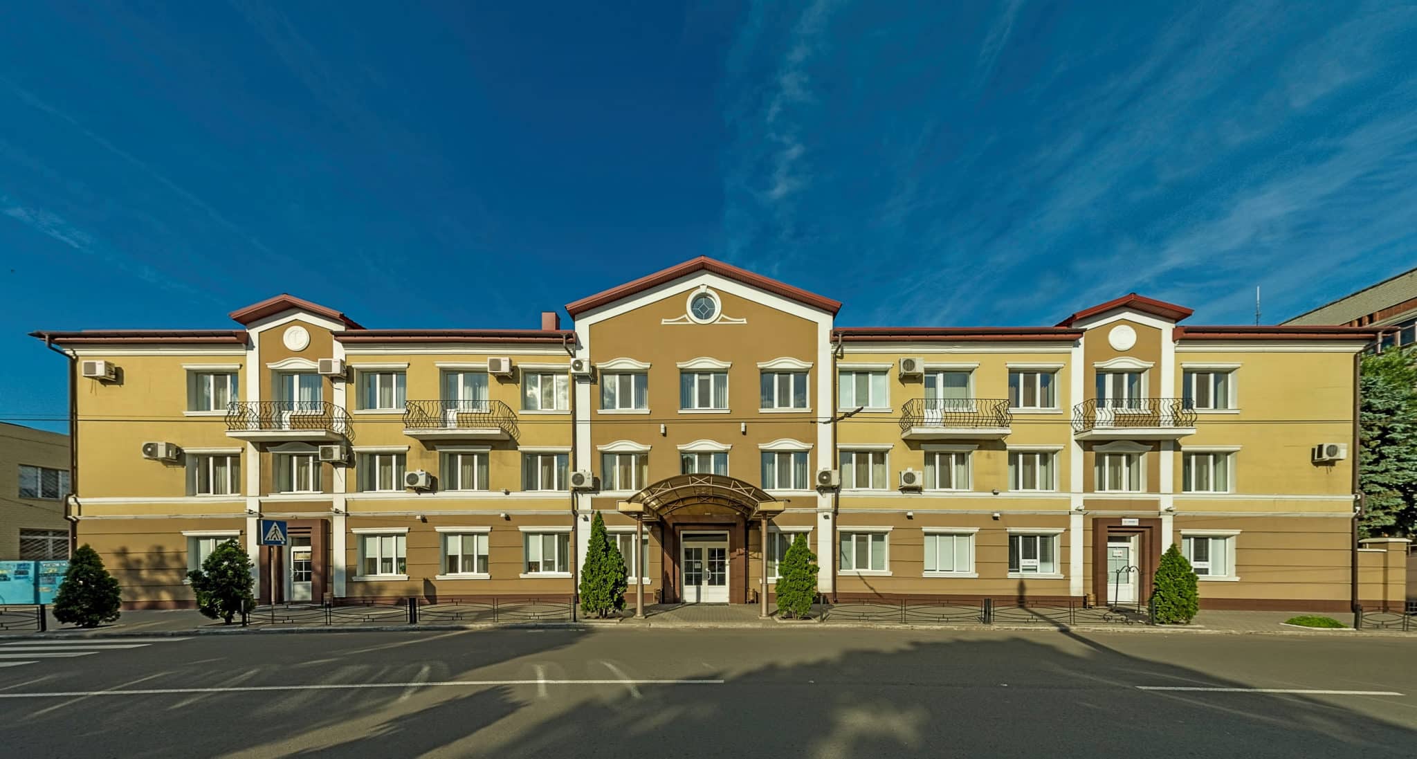 A three-story commercial building with a large parking lot and multiple suites against a clear blue sky.