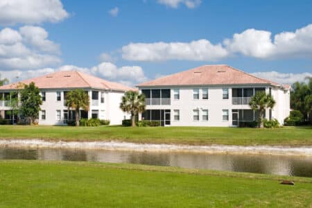 Two large multi-family properties buildings sit on a green lawn with a small creek running across.